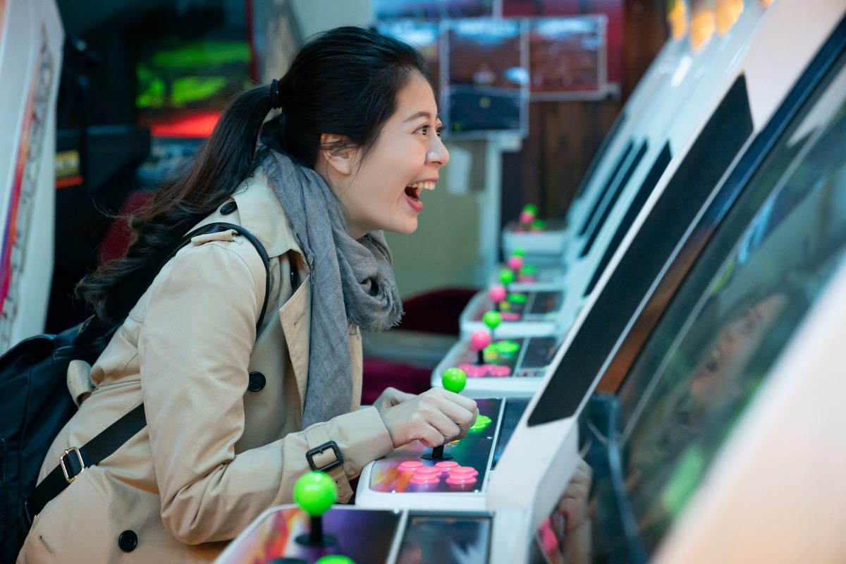 side view of excited Asian Japanese girl having fun playing arcade video games at a store in shinsekai Osaka japan. she holds the joystick of the machine and shouts in excitement