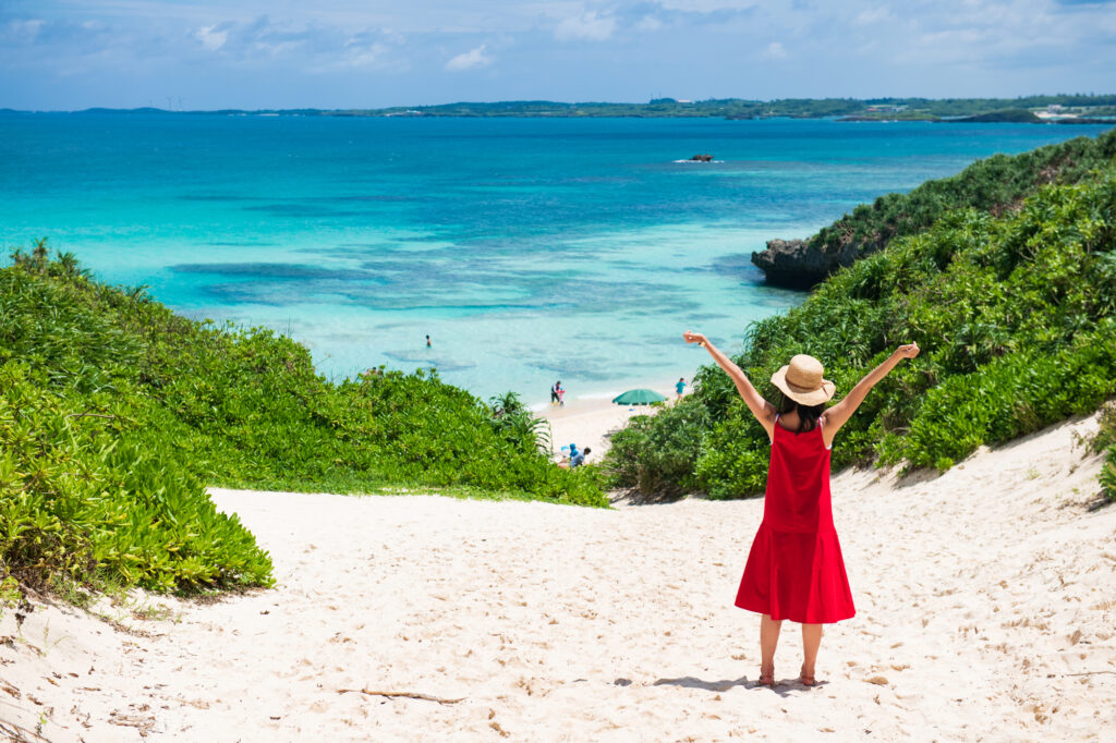 ビーチを見ながら両手を上げる赤いワンピースの女性
