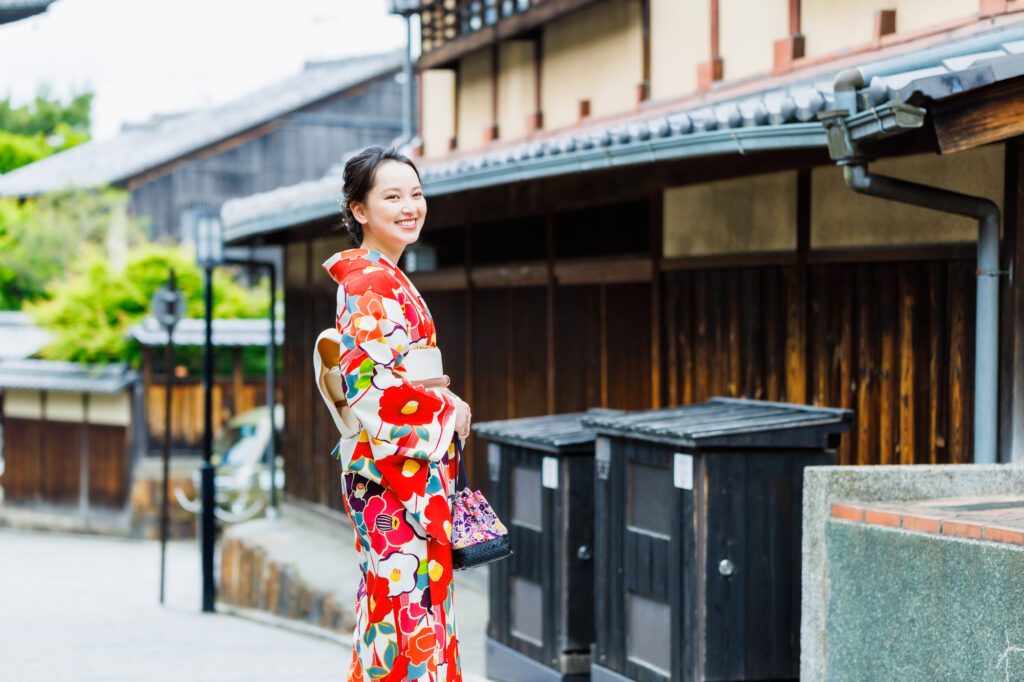 京都の街並みを背景に着物を着た女性が笑顔で佇む