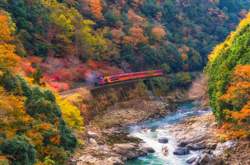色とりどりの紅葉が彩る保津峡。トロッコ列車や保津川下りを楽しむ人々。